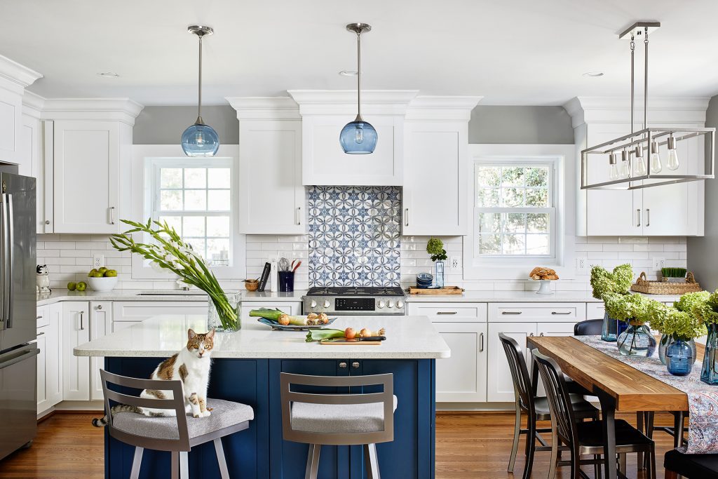 large kitchen remodeling in Virginia with white marble countertop and blue cabinets underneath kitchen island with blue glass shade light fixtures above and wooden 6 chairs table with pendant with 5 light kitchen linear pendant above.