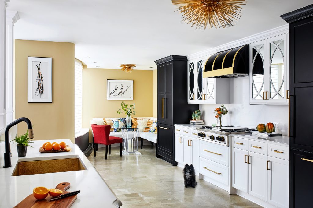 white and gold kitchen with black range hood, cabinets with brass pulls paired with marble countertops