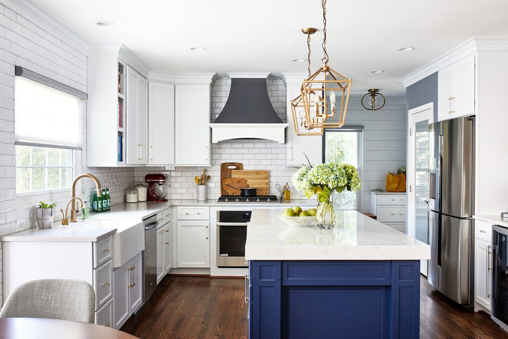 large white top kitchen island with blue draws, two gold glass light pendant, large white cabinets and large farmhouse sink